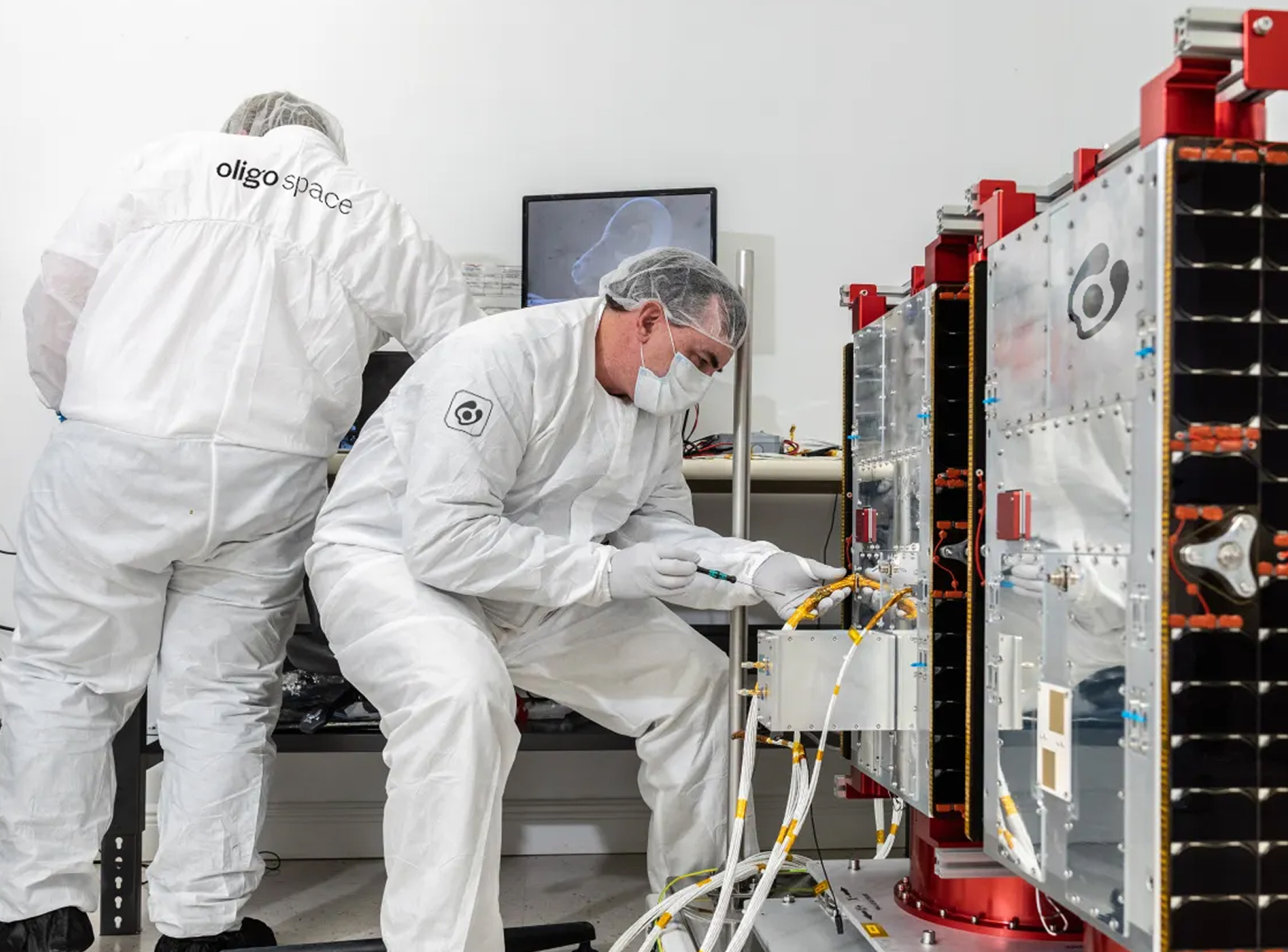 Technicians in cleanroom suits working on a satellite